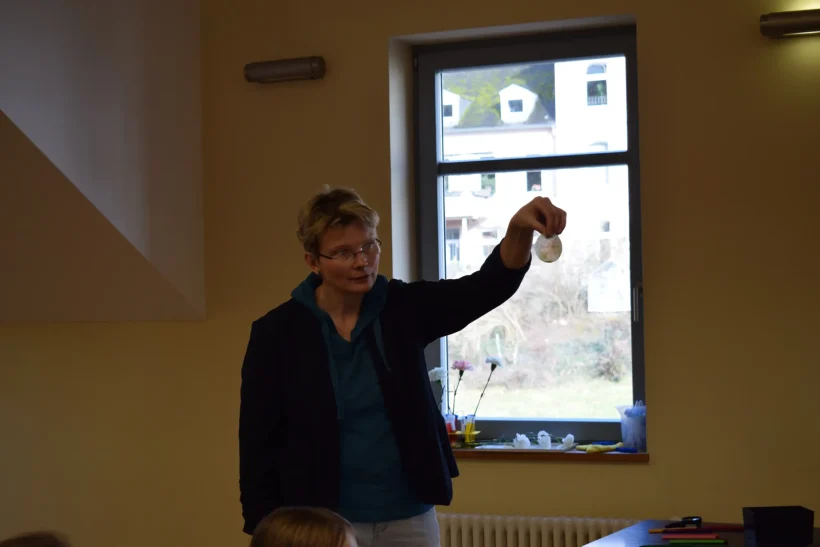 Farbenworkshop Eine Person hält einen Gegenstand hoch, im Hintergrund ein Fenster mit Ausblick.