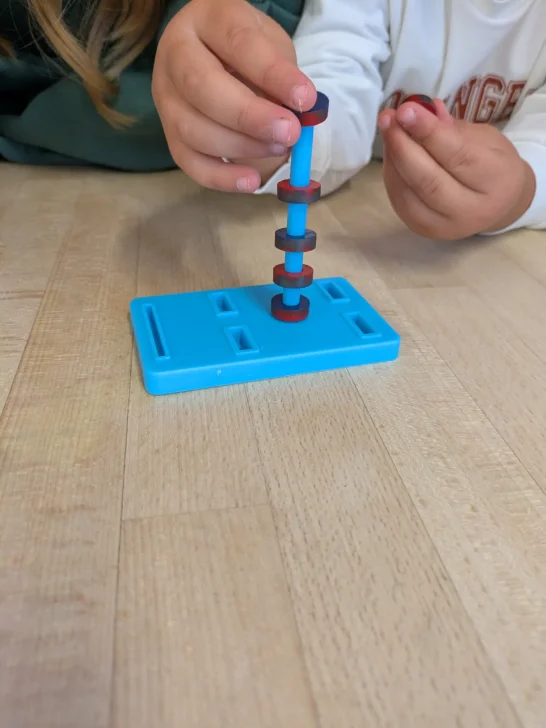 Magnetismus Zwei Hände stapeln bunte Magnete auf einer blauen Säule.