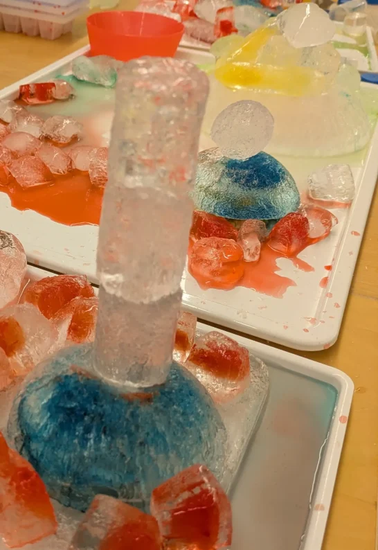 Bauen mit Eis Bunte Eisformen in verschiedenen Farben auf einem Tisch mit geschmolzenem Eis.